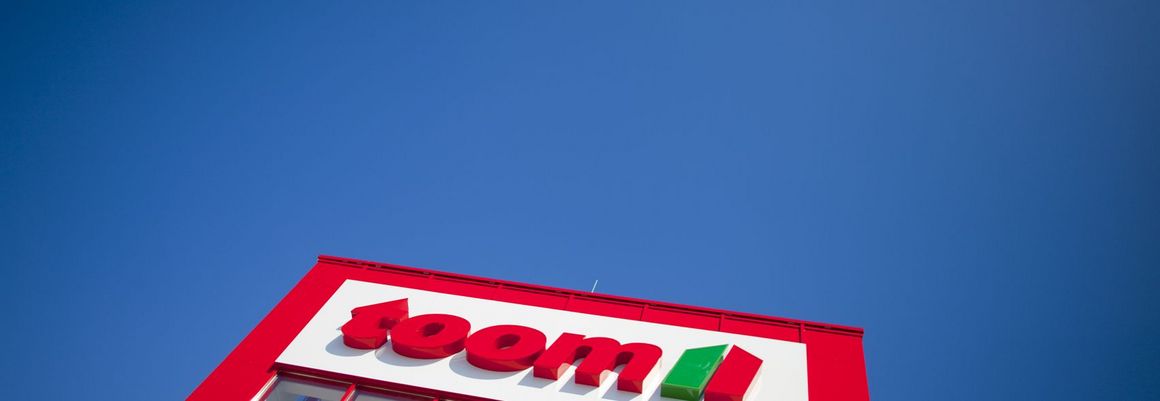 Rote Fassade eines Geschäfts mit Firmenlogo vor blauem Himmel